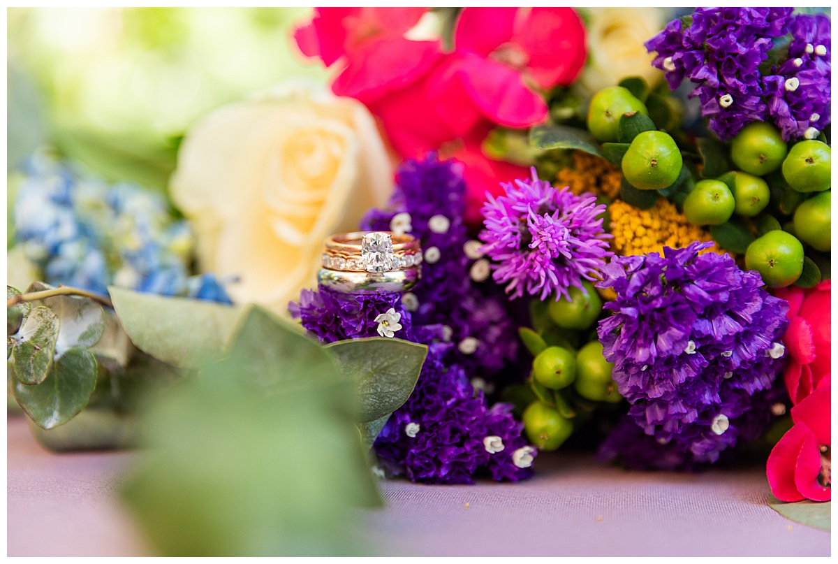 A close up of the couple's rings in the bride's bouquet. The bouquet has lots of colors including: purple, light blue, bright pink, yellow, white, and green.