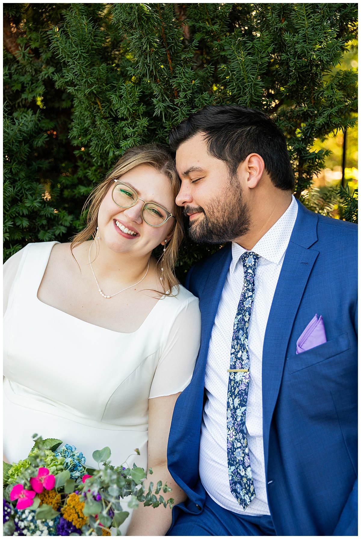 The bride smiles up at the camera while the groom cuddles into her at their Denver Botanic Gardens wedding.