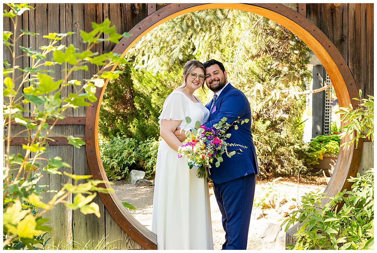 The bride and groom pose in the Asian garden. They are standing under a large wooden circle arch.