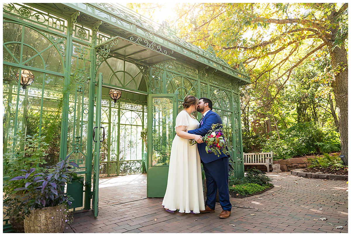 The bride and groom enjoy the last moments of their wedding day in front of the green metal and glass woodland mosaic solarium.