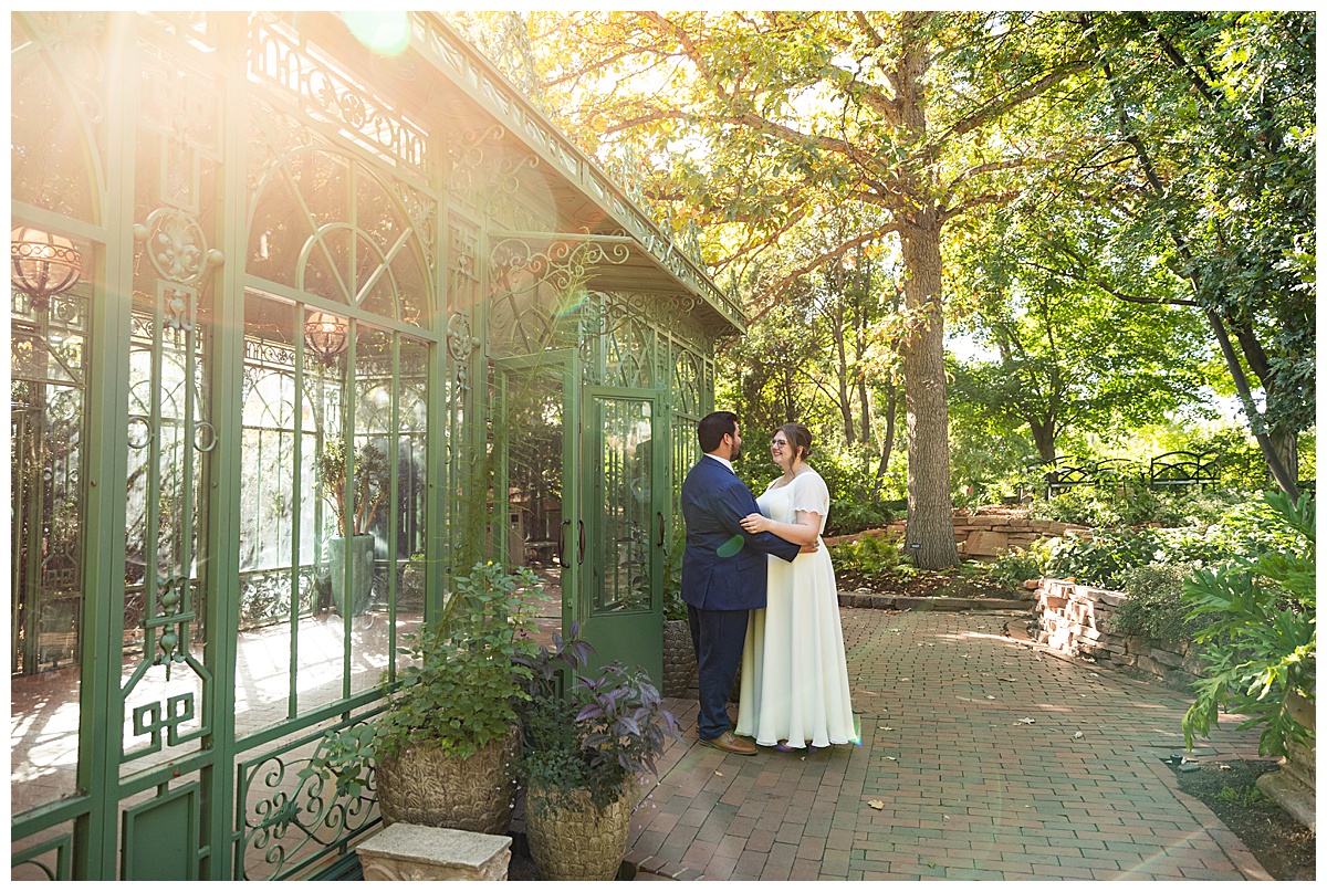 The bride and groom enjoy the last moments of their wedding day in front of the green metal and glass woodland mosaic solarium.