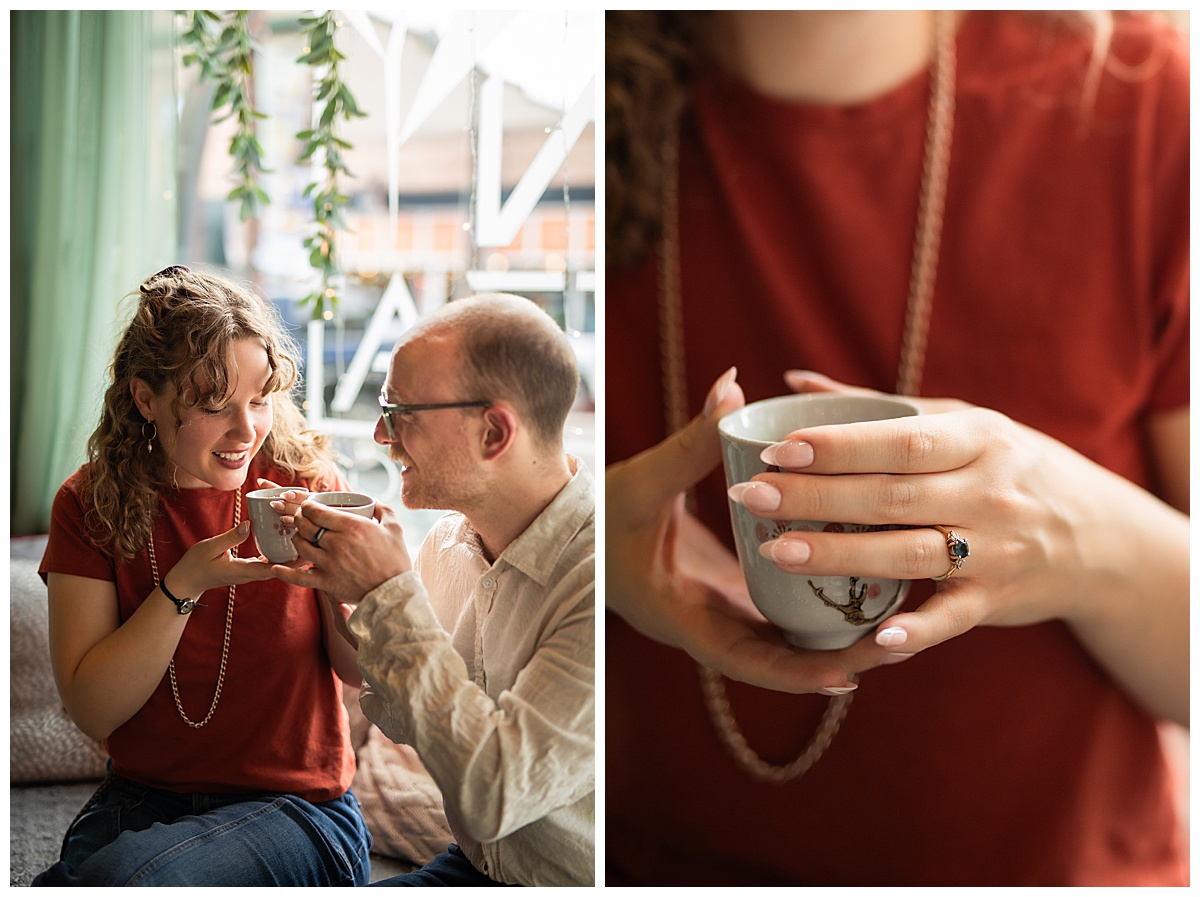 Lily & Cody enjoy tea sitting on a couch by a window. Lily has curly brown hair and is wearing a red shirt and jeans. Cody is wearing glasses with a cream button down shirt and jeans.