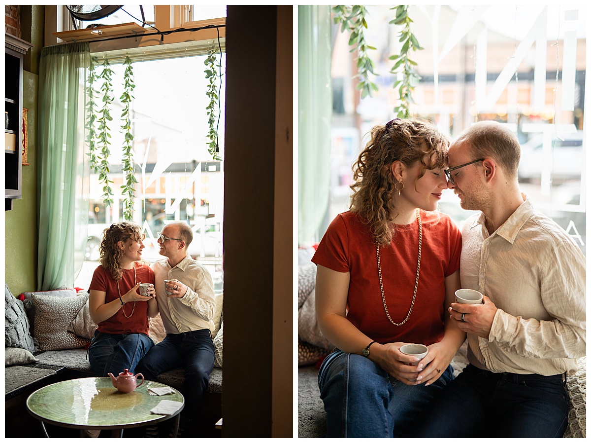 Lily & Cody enjoy tea sitting on a couch by a window. Lily has curly brown hair and is wearing a red shirt and jeans. Cody is wearing glasses with a cream button down shirt and jeans.