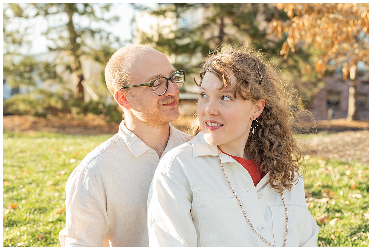 Lily & Cody sit on the grass of Bega Park. Lily has curly brown hair and is wearing a red shirt, a cream jacket, and jeans. Cody is wearing glasses with a cream button down shirt and jeans.