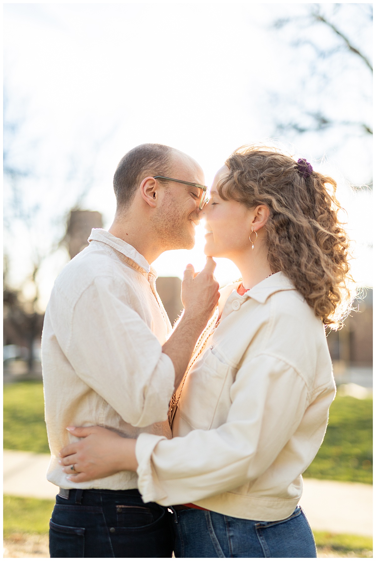 Lily & Cody pose in Bega Park. Lily has curly brown hair and is wearing a red shirt, a cream jacket, and jeans. Cody is wearing glasses with a cream button down shirt and jeans.