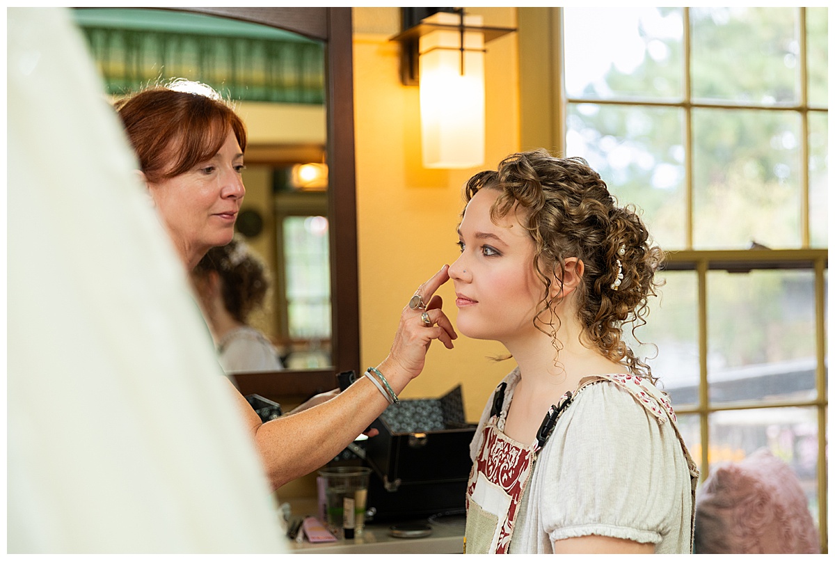 Photo of the bride getting her makeup done. She has curly dirty brown hair pulled up in an updo.
